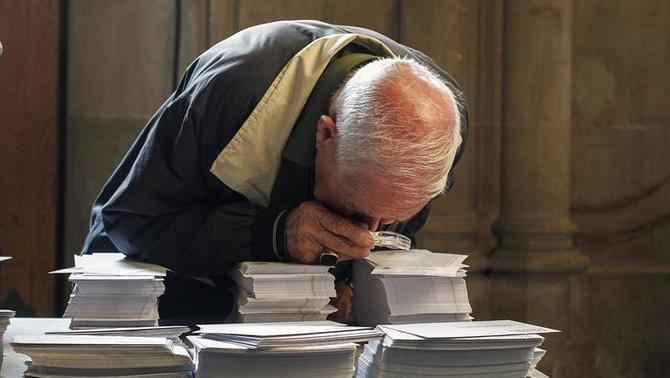 Un hombre observa con una lupa las papeletas de las diferentes formaciones que participan en las elecciones (EFE)