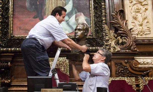 Dos operarios municipales retiran el busto del Rey Juan Carlos I que hay en el Salón de la Reina Regente, donde se celebran los plenos municipales del Ayuntamiento de Barcelona,