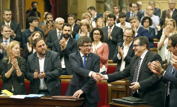 El presidente de la Generalidad, Carles Puigdemont (c), saluda al conseller Jordi Jané en el pleno Parlament, mientras los diputados de Junts pel Sí (JxS).. Efe