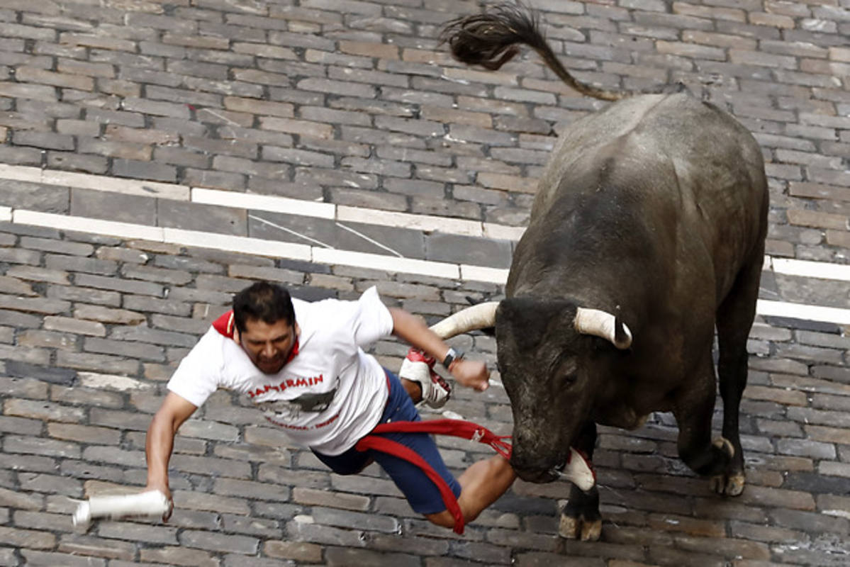 Un mozo cae en la curva de Mercaderes ante un toro de la ganadería abulense de José Escolar Gil, en el tercer encierro de los Sanfermines 2016. Efe