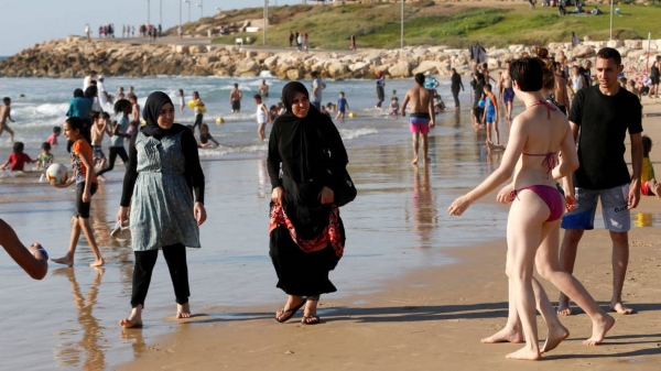 Mujeres musulmanas caminan por la playa sorprendida ante dos mujeres en bikini de playa. Archivo Reuters.