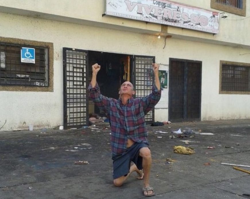 FOTOGRAFÍA. CIUDAD DEL BOLÍVAR (VENEZUELA),17.12.2016. Un propietario de la tienda 'Víveres 88' pide la ayuda de Dios, impotente ante el saqueo de su tienda en la luz del día. Ñ Pueblo