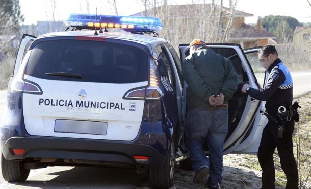Un agente de la Policia Municipal de Valladolid introduce en el coche patrulla a uno de los detenidos por el tiroteo producido este mediodía en un pinar... Efe