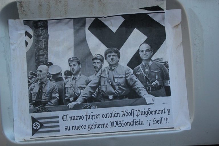 FOTOGRAFÍA. CONSULADO DE ALEMANIA EN BARCELONA (CATALUÑA) REINO DE ESPAÑA, 20/07/2018. Un disidente catalán aparca su pequeña furgoneta al frente del consulado de Alemania en Barcelona (Reino de España) con una "divertida fotografía" del régimen nazi de la genestapo de la "República Catalana", donde aparecen los presos fascistas de régimen nacionalsocialista amarillo: exconsejeros, Jordi Turull Negre (derecha), el líder del primer imperio fascista catalán, Carles Puigdemont Casamajó (2º a la derecha), Oriol Junqueras Vies, vicepresidente y líder de la ultraizquierda separatista Esquerra Republicana de Cataluña (ERC) (3º derecha), el consejero Raül Romeva Roure (4º derecha), el líder de la "banda criminal infiltrada" en los Mozos de Escuadra, Josep Lluís Trapero (2º plano entre Junqueras y Puigdemont), durante un mitin fascista en Cataluña, antes de la huida y de la caída de la genestapo en las operaciones de la Guardia Civil y Cuerpo Nacional de Policía del Reino de España. Lasvocesdelpueblo (Ñ Pueblo)