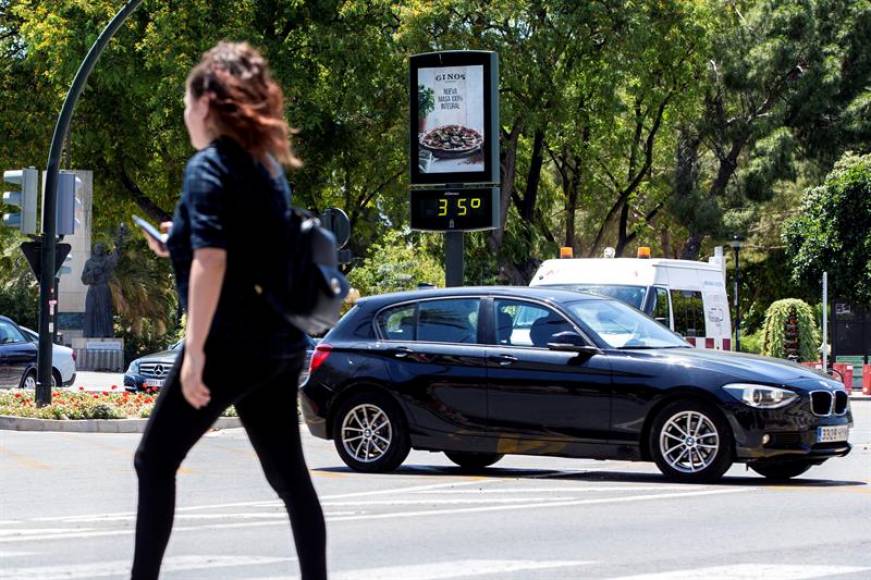 CATALUÑA (ESPAÑA), 10.08.2018. UN TERMÓMETRO MARCA 35º en Cataluña cuando una mujer, en primer plano, pasea con un pantalón negro mirando su teléfono móvil. 11 personas que han fallecido. Efe