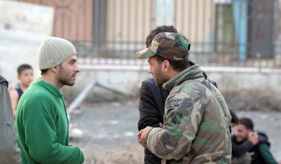 Hombres armados hablan con soldados sirios cerca de los autobuses del Gobierno en el campo de Damasco, Siria, poco antes de ser transportados a la ciudad nororiental de Idleb. Efe