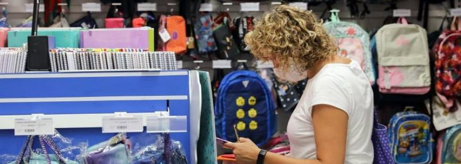 FOTOGRAFÍA. ESPAÑA, 22.08.2020. Una mujer, preparada con una lista de material escolar, consulta el precio, en una papelería, de una mochila infantil. Efe