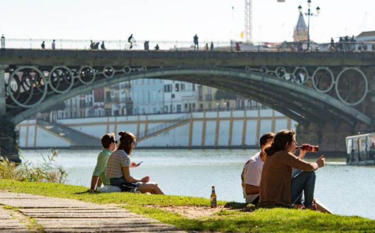 FOTOGRAFÍA. SEVILLA (ANDALUCÍA) REINO DE ESPAÑA, 29.10.2020. Varias personas se relajan este lunes en la orilla del Guadalquivir junto al Puente de Triana de Sevilla. Efe 