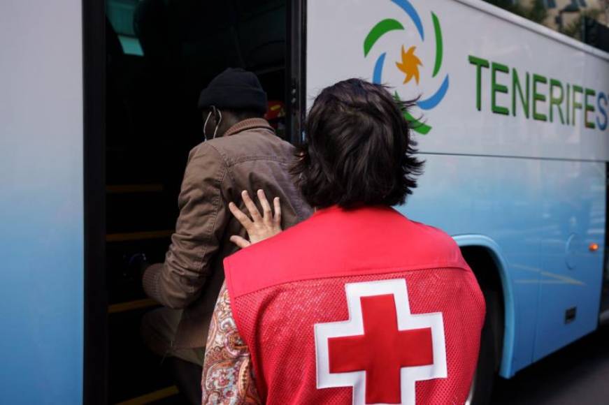 FOTOGRAFÍA. CANARIAS (ESPAÑA), 16.03.2021. Un voluntario de Cruz Roja ayuda a uno de los inmigrantes a subir al autobús. Efe