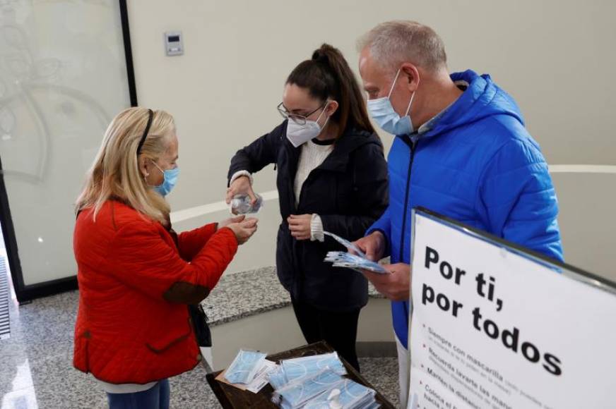 FOTOGRAFÍA. MADRID (ESPAÑA), 04.05.2021. Una mujer ofrece gel hidroalcohólico a los votantes a la entrada del colegio La Inmacualada-Marillac en Madrid. Efe