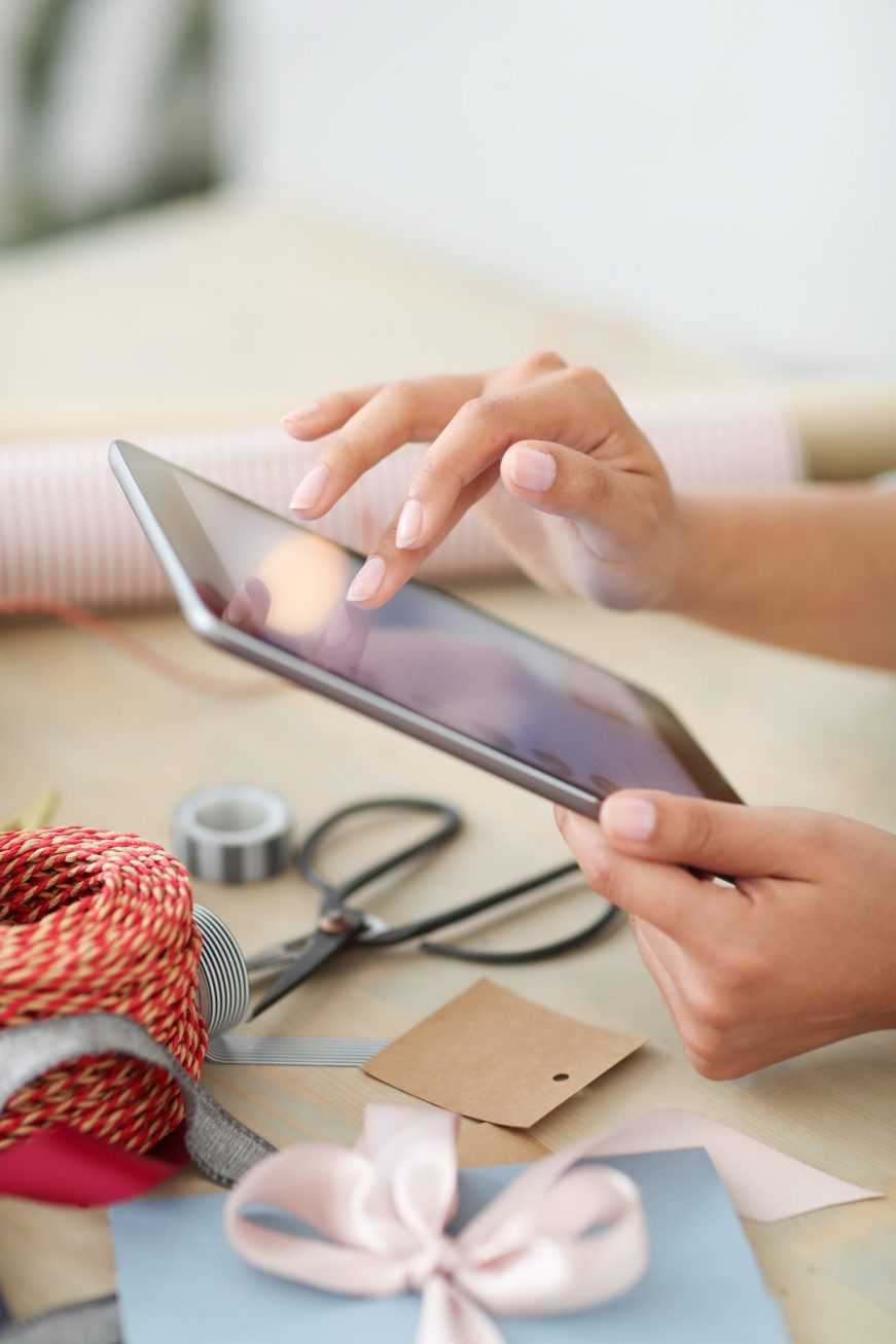 FOTOGRAFÍAN. MUNDO, DICIEMBRE 2020. Una mujer joven envolviendo regalos de navidad, consultando su correo electrónico en un teléfono smartphone. Imagen creada por Freepik