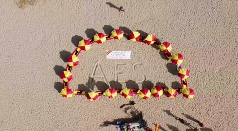 FOTOGRAFÍA. ARENYS DE MAR (BARCELONA) REINO DE ESPAÑA, 11 DE JULIO DE 2021. Los plantan sombrillas españolas en la Playa del Cavalló de Arenys de Mar (Barcelona) como rechazo a los indultos al procés, con un mensaje contundente que dice «Arriba España (AES)». Temperaturas, playa, España, lluvias, calor, bandera, resistencia. Lasvocesdelpueblo (Ñ pueblo)