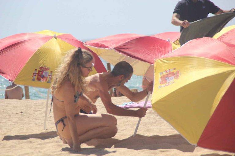 FOTOGRAFÍA. PREMIA DE MAR (BARCELONA) ESPAÑA, 05 DE AGOSTO DE 2023. Varios vecinos catalanes participan en una plantada de sombrillas de colores y simbolos institucionales del Reino de España en la playa de Premia de Mar (barcelona), formando la letra «Ñ» y dejando un claro mensaje al nuevo Gobierno de España que previsiblemente necesitará los síes del partido del prófugo d ela Justicia y golpista Carles Puigdemont Casamajò, Juntos por Cataluña (JxCat). Temperaturas. Lasvocesdelpueblo (Ñ Pueblo)