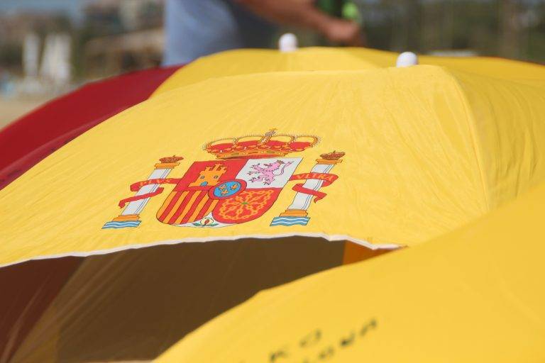 FOTOGRAFÍA. PREMIA DE MAR (BARCELONA) ESPAÑA, 05 DE AGOSTO DE 2023. Cielos poco nubosos o despejados en España. Varios vecinos catalanes participan en una plantada de sombrillas de colores y simbolos institucionales del Reino de España en la playa de Premia de Mar (barcelona), formando la letra «Ñ» y dejando un claro mensaje al nuevo Gobierno de España que previsiblemente necesitará los síes del partido del prófugo d ela Justicia y golpista Carles Puigdemont Casamajò, Juntos por Cataluña (JxCat). Temperaturas. Lasvocesdelpueblo (Ñ Pueblo)