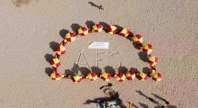 FOTOGRAFÍA. ARENYS DE MAR (BARCELONA) REINO DE ESPAÑA, 11 DE JULIO DE 2021. Temperaturas de 36 y 38 grados en España.- Los plantan sombrillas españolas en la Playa del Cavalló de Arenys de Mar (Barcelona) como rechazo a los indultos al procés, con un mensaje contundente que dice «Arriba España (AES)». Temperaturas, playa, España, lluvias, calor, bandera, resistencia. Lasvocesdelpueblo (Ñ pueblo)