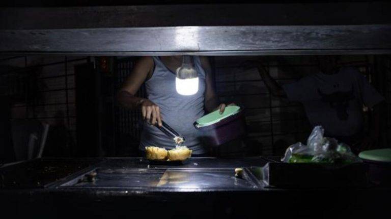 FOTOGRAFÍA. MARACAIBO (VENEZUELA), 29 DE 02 DE 2024. Venezuela sin luz.- Una persona vende comida ayudado con un bombillo en medio de la oscuridad durante un corte eléctrico, el 29 de febrero de 2024 en Maracaibo. Efe