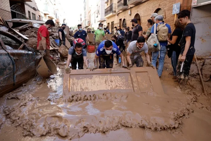 FOTOGRAFÍA. PAIPORTA (VALENCIA) COMUNIDAD VALENCIANA) REINO DE ESPAÑA, 02 DE NOVIEMBRE DE 2024. Varias personas retiran el lodo acumulado en una calle de la localidad valenciana de Paiporta. Una mujer cruza una calle de la localidad de Masanasa, en Valencia. La Comunitat Valenciana intenta recuperarse de la peor Depresión Aislada en Niveles Altos (DANA) del siglo en España, que ha dejado más de dos centenares de muertos en esa región, además de un inmenso escenario de daños en carreteras, calles e infraestructuras de numerosas localidades. Una DANA tras fuertes lluvias torrenciales y golpear muy fuertemente al reino de España, con epicentro en la provincia de Valencia (Comunidad Valenciana) donde se ha registrado ya 211 muertos, como cifra provisional para este sábado 2 de noviembre de 20224, y con menos dureza en la provincia de Málaga (Andalucía) y en la región de Castilla-La Mancha. La devastación de los efectos de la DANA que arrasó este martes la provincia de Valencia dejó decenas de personas fallecidas -70 contabilizadas hasta las 16.00 horas-, la angustia de quienes no pueden contactar con sus familiares desde ayer e imágenes desoladoras de la destrucción que han dejado a su paso las inundaciones. En medio de la tragedia, que ha llevado a activar el protocolo de Múltiples Víctimas para identificar a los fallecidos, las autoridades combaten este miércoles un "nuevo enemigo": los bulos que alertan de supuestas evacuaciones, desbordamientos o la caída del 112, que interrumpen la labor de los servicios de emergencias. La ciudadanía de la provincia ha recibido a primera hora de esta mañana de nuevo en sus móviles un mensaje del sistema Es-Alert para evitar cualquier tipo de desplazamiento por las carreteras de la provincia, muchas de cuales permanecen cortadas e impiden todavía acceder a las zonas más afectadas. Efe