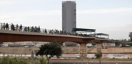 FOTOGRAFÍA. LA TORRE (VALENCIA) COMUNIDAD VALENCIANA (REINO DE ESPAÑA), 01 DE NOVIEMBRE DE 2024. Cientos de personas cruzan la pasarela que da acceso al barrio de La Torre, en Valencia, este viernes. La Comunitat Valenciana intenta recuperarse de la peor Depresión Aislada en Niveles Altos (DANA) del siglo en España, que ha dejado más de dos centenares de muertos en esa región, además de un inmenso escenario de daños en carreteras, calles e infraestructuras de numerosas localidades. Una DANA tras fuertes lluvias torrenciales y golpear muy fuertemente al reino de España, con epicentro en la provincia de Valencia (Comunidad Valenciana) donde se ha registrado ya 202 muertos, como cifra provisional para este viernes 1 de noviembre de 20224, y con menos dureza en la provincia de Málaga (Andalucía) y en la región de Castilla-La Mancha. La devastación de los efectos de la DANA que arrasó este martes la provincia de Valencia dejó decenas de personas fallecidas -70 contabilizadas hasta las 16.00 horas-, la angustia de quienes no pueden contactar con sus familiares desde ayer e imágenes desoladoras de la destrucción que han dejado a su paso las inundaciones. En medio de la tragedia, que ha llevado a activar el protocolo de Múltiples Víctimas para identificar a los fallecidos, las autoridades combaten este miércoles un "nuevo enemigo": los bulos que alertan de supuestas evacuaciones, desbordamientos o la caída del 112, que interrumpen la labor de los servicios de emergencias. La ciudadanía de la provincia ha recibido a primera hora de esta mañana de nuevo en sus móviles un mensaje del sistema Es-Alert para evitar cualquier tipo de desplazamiento por las carreteras de la provincia, muchas de cuales permanecen cortadas e impiden todavía acceder a las zonas más afectadas. Efe