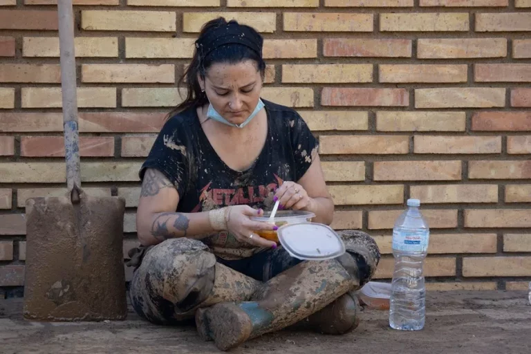 FOTOGRAFÍA. PAIPORTA (VALENCIA) COMUNIDAD VALENCIANA (REINO DE ESPAÑA), 02 DE NOVIEMBRE DE 2024. Una mujer come en una acera llena de lodo.  Varias personas retiran el lodo acumulado en una calle de la localidad valenciana de Paiporta (Valencia) Comunidad Valenciana, este sábado, 2 de noviembre de 2024, tras la Depresión Aislada en Niveles Altos (DANA) o (gota fría). Efe 