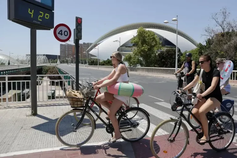 FOTOGRAFÍA. REINO DE ESPAPAÑA, 01 DE JULIO DE 2025. Varias jóvenes transportan sus flotadores en bici al paso de un termómetro que marca 42 grados centígrados durante este martes en plena ola de calor, coincidiendo hoy -1 de julio- con la operación salida de vacaciones de verano para muchos, en el que la jornada será sofocante, con 43 grados en puntos de Andalucía y más de 40 grados en amplias zonas del país por el actual episodio de temperaturas extremas, que durará al menos hasta el jueves. Efe