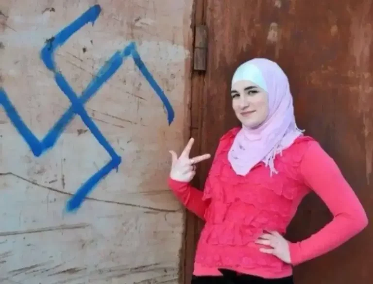 FOTOGRAFÍA. MUNDO ANTISEMITA ÁRABE, 08 DE AGOSTO DE 2025. Una joven mujer musulmana posa junto al símbolo nazi, conocido como las "Schutzstaffel", en español "Escuadrón de Protección", abreviado "SS" y estilizado durante su existencia con las runas armanas "ᛋᛋ" —símbolo de una organización paramilitar, policial, política, penitenciaria y de seguridad al servicio del líder del Tercer Reich de la Alemania nazi, Adolf Hitler, y del Partido Nacionalsocialista Obrero Alemán (NSDAP), una formación de izquierda en la Alemania nazi, y después por toda la Europa ocupada por los nazis durante la Segunda Guerra Mundial. Sana Ebrahimi/Lasvocesdelpueblo (Ñ Pueblo)