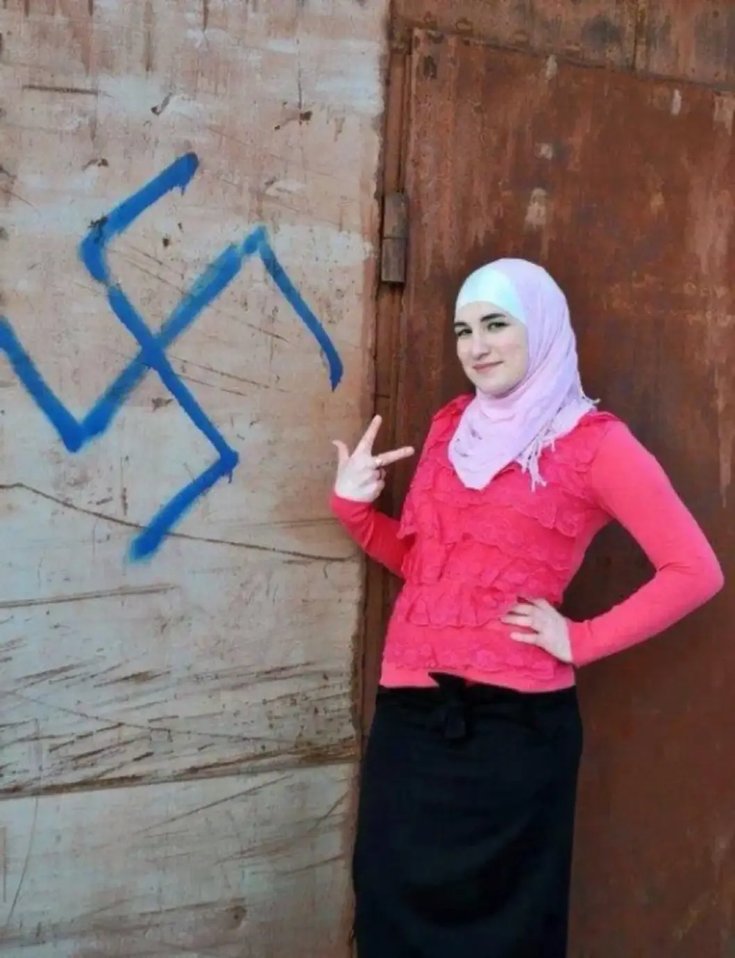 FOTOGRAFÍA. MUNDO ANTISEMITA ÁRABE, 08 DE AGOSTO DE 2025. Una joven mujer musulmana posa junto al símbolo nazi, conocido como las "Schutzstaffel", en español "Escuadrón de Protección", abreviado "SS" y estilizado durante su existencia con las runas armanas "ᛋᛋ" —símbolo de una organización paramilitar, policial, política, penitenciaria y de seguridad al servicio del líder del Tercer Reich de la Alemania nazi, Adolf Hitler, y del Partido Nacionalsocialista Obrero Alemán (NSDAP), una formación de izquierda en la Alemania nazi, y después por toda la Europa ocupada por los nazis durante la Segunda Guerra Mundial. Sana Ebrahimi/Lasvocesdelpueblo (Ñ Pueblo)