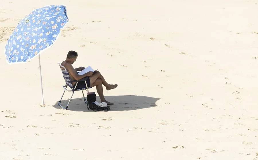 SAN SEBASTIÁN (LAS VASCONGADAS) REINO DE ESPAÑA, 07 DE AGOSTO DE 2025. Un hombre lee bajo su sombrilla en la orilla de la playa de La Concha de San Sebastián, las Vascongadas (Reino de España). Efe