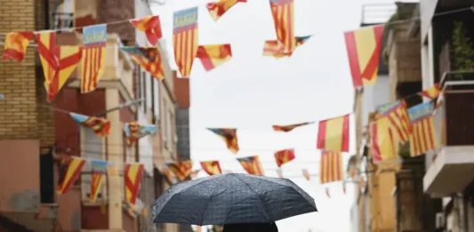 FOTOGRAFÍA. CATARROJA (VALENCIA) REINO DE ESPAÑA, 09 DE OCTUBRE DE 2025. Un hombre pasa con un paraguas bajo los banderines colgados en Catarroja (Valencia), este 9 de octubre, Día de la Comunidad Valenciana. Efe