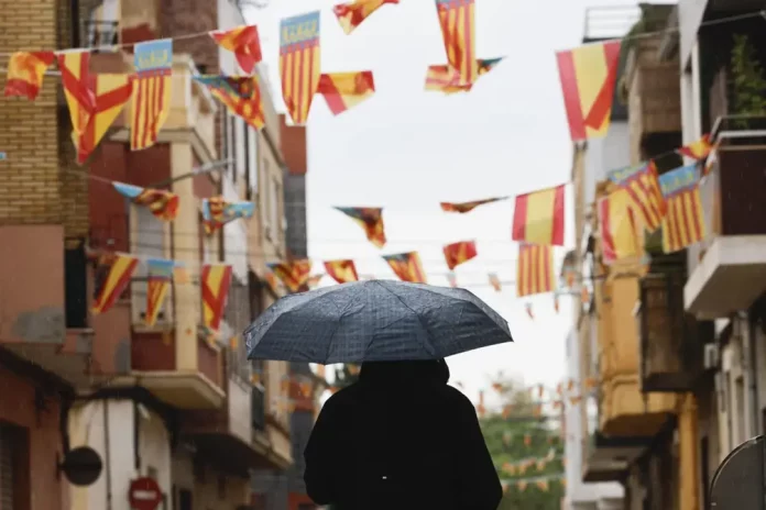 Aviso naranja por lluvias en Comunidad Valenciana; Murcia y Baleares FOTOGRAFÍA. CATARROJA (VALENCIA) REINO DE ESPAÑA, 09 DE OCTUBRE DE 2025. Un hombre pasa con un paraguas bajo los banderines colgados en Catarroja (Valencia), este 9 de octubre, Día de la Comunidad Valenciana. Efe