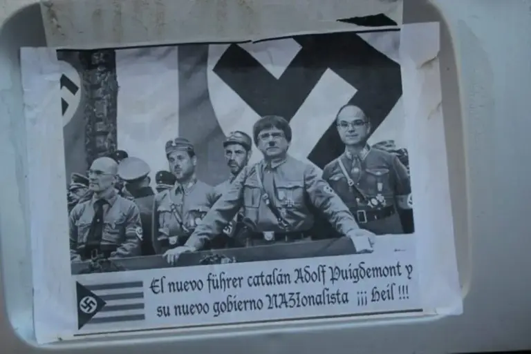 FOTOGRAFÍA. CONSULADO DE ALEMANIA EN BARCELONA (CATALUÑA) REINO DE ESPAÑA, 20/07/2018. Un disidente catalán aparca su pequeña furgoneta al frente del consulado de Alemania en Barcelona (Reino de España) con una "divertida fotografía" del régimen nazi de la genestapo de la "República Catalana", donde aparecen los presos fascistas de régimen nacionalsocialista amarillo: exconsejeros, Jordi Turull Negre (derecha), el líder del primer imperio fascista catalán, Carles Puigdemont Casamajó (2º a la derecha), Oriol Junqueras Vies, vicepresidente y líder de la ultraizquierda separatista Esquerra Republicana de Cataluña (ERC) (3º derecha), el consejero Raül Romeva Roure (4º derecha), el líder de la "banda criminal infiltrada" en los Mozos de Escuadra, Josep Lluís Trapero (2º plano entre Junqueras y Puigdemont), durante un mitin fascista en Cataluña, antes de la huida y de la caída de la genestapo en las operaciones de la Guardia Civil y Cuerpo Nacional de Policía del Reino de España. Lasvocesdelpueblo (Ñ Pueblo)
