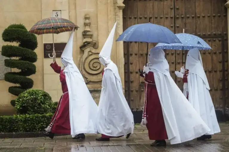 FOTOGRAFÍA. CÓRDOBA (ANDALUCÍA) REINO DE ESPAÑA, 25 DE MARZO DE 2024. Martes Santo de chubascos y lluvias en toda España. Semana Santa. Unos nazarenos de la Hermandad de La Sentencia se protegen de la lluvia con paraguas mientras caminan hacia su templo este lunes en Córdoba. Efe
