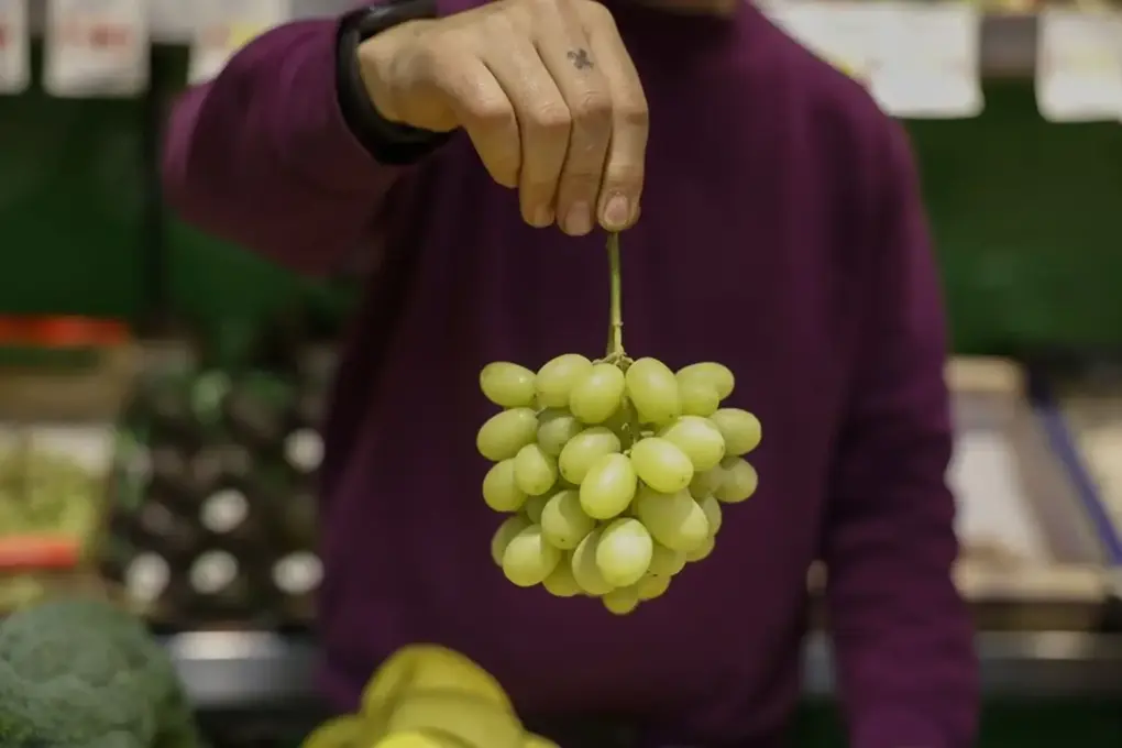 FOTOGRAFÍA. MADRID (ESPAÑA), 27 DE DICIEMBRE DE 2025.12 Campanadas: Las uvas han subido un 40 %. Un frutero muestra un racimo de uvas en un mercado de Madrid. Efe