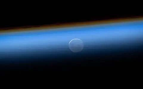 FOTOGRAFÍA. ESPACIO (MÁS ALLÁ DE LA ATMÓSFERA TERRESTRE), 07 DE ABRIL DE 2026. Comunicación entre Estación Espacial y Artemis II: hito histórico para la NASA. En esta fotografía tomada desde la Estación Espacial Internacional el 27 de mayo de 2025, se observa la Luna Nueva aparentemente debajo de la atmósfera terrestre durante una puesta de sol orbital. Nasa/Lasvocesdelpueblo (Ñ Pueblo)