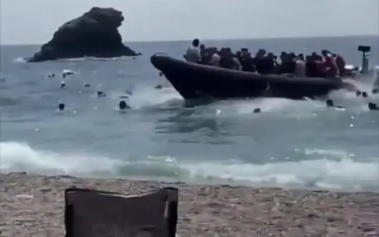 FOTOGRAFÍA. CARTAGENA (REGIÓN DE MURCIA) ESPAÑA, 21 DE AGOSTO DE 2026. Una lanchas rápidas (patera) con varias decenas de inmigrantes ilegales magrebíes, desembarca en la cala del Barco de Cartagena ante varios turistas y vecinos de Murcia, entre ellos muchos en el miedo que abandonaron el lugar corriendo. Los ilegales magrebíes desaparecieron por la ciudad, respondiendo a la llamada del Gobierno mugracionsista de España en coalición del Partido Socialista (PSOE) y Movimiento Sumar, con Pedro Sánchez Pérez-Castejón al frente, de una regularización masiva de los indocumentados en el país. la llamada de fronteras abiertas de España del PSOE y Sumar, apoyada por Podemos, llegó correctamente a los destinarios que ahora están llegando en masas por todas partes. Captura vídeo de testigos/Lasvocesdelpueblo (Ñ Pueblo)
