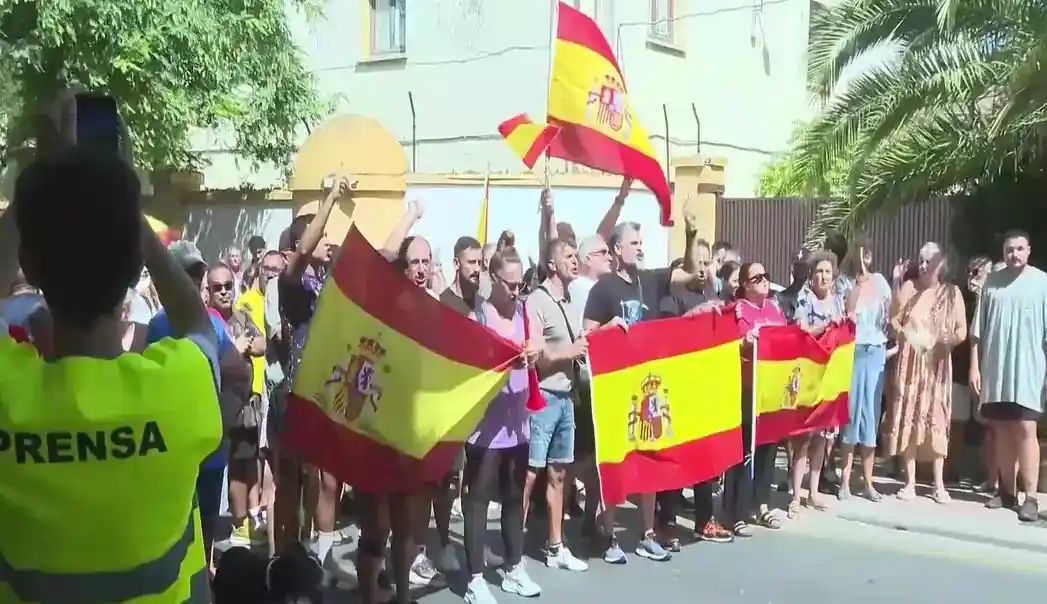 FOTOGRAFÍA. CEUTA (ESPAÑA), 25 DE AGOSTO DE 2026. Ceuta protesta contra acogida de inmigrantes: invasores deportación; invasores expulsión. Varios cientos de vecinos de Ceuta han trasladado este martes hasta la plaza de los Reyes, frente a la Delegación del Gobierno, la protesta contra el posible alojamiento de inmigrantes ilegales -"invasores", apuntan los manifestantes visiblemente hartos y muy desamparados ante la inacción completa de las autoridades locales y nacionales- en distintos puntos de la ciudad, después de que una concentración iniciada en la zona del Fischer se haya convertido en una movilización ciudadana. Lasvocesdelpueblo (Ñ Pueblo)