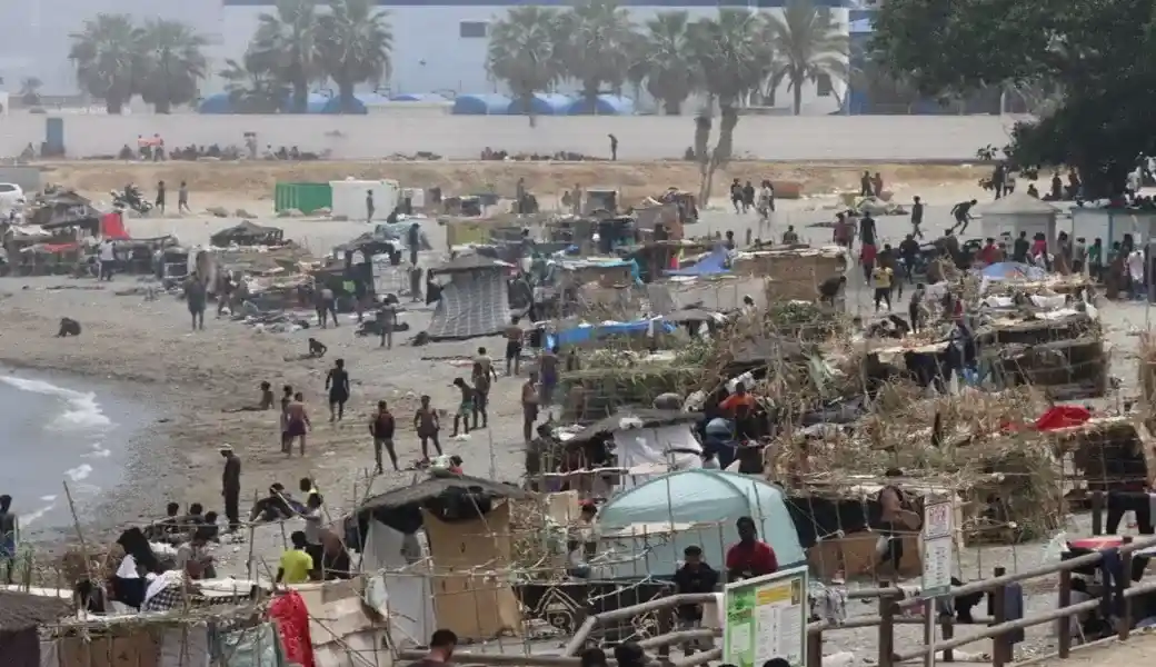 FOTOGRAFÍA. CEUTA (ESPAÑA), 19 DE AGOSTO DE 2026. En la imagen, centenares de los invasores inmigrantes ilegales marroquíes del asalto masivo a la frontera marítima y terrestre de España en Ceuta, acampados en la Playa del Trampolín de la Ciudad Autónoma de Ceuta, exigiendo ser acogido por España y ser traslados a la Península en hoteles con pensión y papeles. Y es que varios de los asaltantes amenazan con que han iniciado una huelga de hambre para obligar al Gobierno de Pedro Sánchez Pérez-Castejón a atender sus exigencias de acogida y regularización masiva. Efe