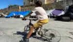 FOTOGRAFÍA. CEUTA (ESPAÑA), 26 DE AGOSTO DE 2026. Un inmigrante ilegal marroquí Menor Extranjero No Acompañado (MENA) sobre una bicicleta desvecijada en el campamento de inmigrantes ilegales en la zona de las naves del Tarajal en Ceuta (España). Efe