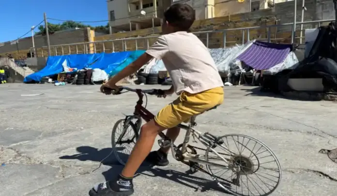 FOTOGRAFÍA. CEUTA (ESPAÑA), 26 DE AGOSTO DE 2026. Un inmigrante ilegal marroquí Menor Extranjero No Acompañado (MENA) sobre una bicicleta desvecijada en el campamento de inmigrantes ilegales en la zona de las naves del Tarajal en Ceuta (España). Efe