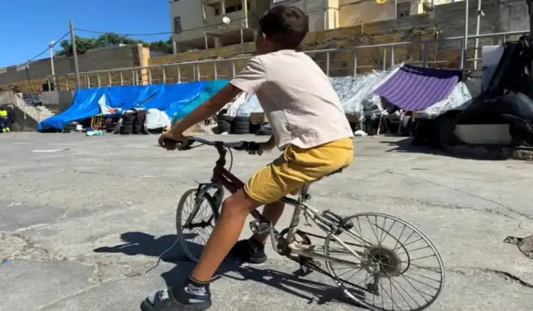 FOTOGRAFÍA. CEUTA (ESPAÑA), 26 DE AGOSTO DE 2026. Un inmigrante ilegal marroquí Menor Extranjero No Acompañado (MENA) sobre una bicicleta desvecijada en el campamento de inmigrantes ilegales en la zona de las naves del Tarajal en Ceuta (España). Efe