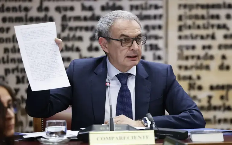 FOTOGRAFÍA. MADRID, 2 DE MARZO DE 2026. El expresidente del Gobierno socialista, José Luis Rodríguez Zapatero, comparece en la comisión de investigación del Senado luciendo traje oscuro, corbata azul y gafas, mientras exhibe ante la mesa un folio manuscrito que sostiene con su mano derecha sobre el cartel oficial que le identifica como «COMPARECIENTE». La imagen recoge el tenso momento de su declaración en la Cámara Alta por sus presuntas vinculaciones en el Caso Plus Ultra, sirviendo como ilustración de portada para el avance judicial contra la corrupción del socialismo bajo el titular: «Anticorrupción acorrala al socialista Zapatero por presunta malversación y contrabando de joyas». EFE