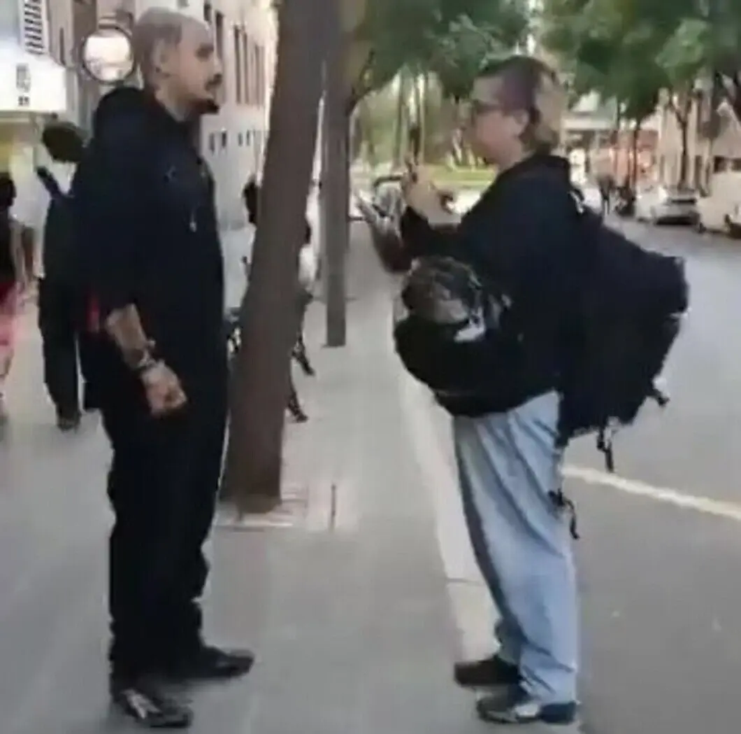 FOTOGRAFÍA. TARRAGONA, 16 D EOCTUBRE DE 2026. Detienen con un cuchillo a los radicales que asaltaron la sede de Vox en Tarragona. La fisonomía de los atacantes pillados in fraganti queda plenamente expuesta: se observa a un varón joven, de estatura media-alta, complexión fuerte, con la cabeza rapada al cero pero con una perilla y barba perfiladas. Viste un uniforme táctico completamente negro compuesto por sudadera con capucha, pantalones anchos y calzado oscuro. Destaca en su brazo derecho un denso tatuaje de mangas oscuras que se extiende hasta la muñeca. A su lado se sitúa la mujer identificada como la agresora del miércoles: de estatura media, complexión estándar, con el pelo rapado por los laterales y un flequillo teñido de rubio platino, portando gafas de montura negra. Luce pantalones de chándal gris claro, calzado oscuro y una voluminosa riñonera cruzada sobre el pecho —donde ocultaba el cuchillo— junto a una mochila escolar colgada a su espalda. La actitud de ambos es de constante vigilancia, manipulando terminales móviles con actitud desafiante ante el entorno. Lasvocesdelpueblo (Ñ Pueblo)