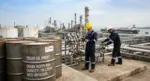 FOTOGRAFÍA. PUERTO DE LA CRUZ, VENEZUELA, VIERNES 9 DE OCTUBRE DE 2026. En primer plano, varios barriles metálicos de almacenamiento de crudo se alinean en los patios de la Refinería de Puerto La Cruz. Al fondo, operarios provistos de cascos y chalecos reflectantes monitorizan el paso del crudo por el entramado de tuberías e imponentes torres de fraccionamiento industrial. La escena ilustra el complejo y tenso equilibrio del sector de los hidrocarburos en una jornada de alta volatilidad internacional por los paros productivos forzados en Occidente y la inestabilidad en Oriente Próximo. IA/Lasvocesdelpueblo (Ñ Pueblo).