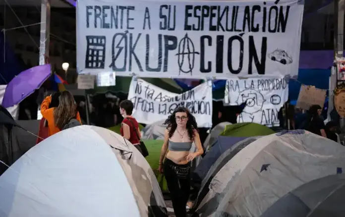 El TSJM dilata el desalojo de la acampada ultraizquierdista en el Sol y da oxígeno al Gobierno FOTOGRAFÍA, MADRID, 05 DE OCTUBRE DE 2026. Una abigarrada multitud de militantes y activistas de ultraizquierda abarrota la totalidad de la remodelada Puerta del Sol de Madrid, concentrándose de manera masiva en las inmediaciones de la Real Casa de Correos. Los manifestantes sostienen en alto una gran pancarta central de lona blanca donde se lee en letras negras y rojas el lema "Derecho a techo: Viva la Okupación y huelga de alquileres contra los rentistas", flanqueada por numerosas banderas de color rojo, símbolos comunistas y enseñas republicanas que ondean sobre las cabezas de la multitud. En el plano medio, se aprecian decenas de tiendas de campaña de estilo "iglú" en tonos verdes, azules y grises, instaladas directamente sobre las losas de granito de la plaza, rodeando las salidas acristaladas de la estación de Cercanías del Sol y la estatua de Carlos III. Rostros de jóvenes y activistas veteranos con megáfonos rompen la línea del fondo, donde varias pancartas secundarias exigen la "Inquiokupación legítima frente a los desahucios" y la "expropiación de fondos buitre", conformando una estampa de ocupación ilegal del espacio público custodiada a la distancia por varias furgonetas azules de las Unidades de Intervención Policial (UIP) de la Policía Nacional. EFE