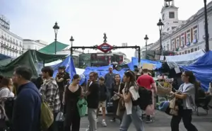 FOTOGRAFÍA. MADRID, 16 DE OCTUBRE DE 2026. Vista de la entrada principal de la estación de Metro de Sol capturada durante las horas previas a la clausura total decretada por la Comunidad de Madrid a causa del grave problema de insalubridad y acumulación de orines provocado por la extrema izquierda. La imagen documenta la degradación total del kilómetro cero de la capital, mostrando el acceso al suburbano completamente sitiado y rodeado por decenas de lonas de plástico azul y verde, estructuras precarias y tiendas de campaña pertenecientes a la acampada ilegal que okupa la plaza desde hace tres semanas. Varios agentes de la Policía Nacional observan la escena en un lateral, mientras un flujo constante de pasajeros, trabajadores y ciudadanos de a pie se ven obligados a sortear los residuos orgánicos, carteles ideológicos y barricadas de los manifestantes antisistema para poder acceder a los andenes, en un ambiente que los informes de riesgos laborales declararon impracticable por los altos niveles de amoníaco detectados en los pozos de ventilación exteriores. EFE