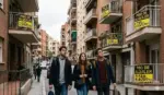 FOTOGRAFÍA. BARCELONA, 07 DE OCTUBRE DE 2026. Un grupo de jóvenes patriotas españoles recorre un barrio residencial de edificios modernos mostrando rostros de profunda preocupación, incertidumbre y desamparo ante la severa crisis de acceso a la vivienda. En la escena, captada en un plano cercano, los jóvenes observan con frustración las fachadas de los inmuebles donde, desde varios de los balcones y ventanas, cuelgan carteles informativos amarillos y negros con el letrero "Piso de alquiler". Los letreros reflejan fielmente el escenario de asfixia y los precios abusivos del mercado actual, mostrando cuotas mensuales drásticamente elevadas y diferenciadas según las características de cada edificio, con cifras visibles que oscilan de forma prohibitiva entre los 1.200 €, 1.800 € y hasta los 2.100 € mensuales. La composición visual resume el drama demográfico y el cuello de botella inmobiliario analizado en el informe de pisos.com, evidenciando cómo la escasez de oferta destruye la capacidad de emancipación de las nuevas generaciones. IA/Lasvocesdelpueblo (Ñ Pueblo)