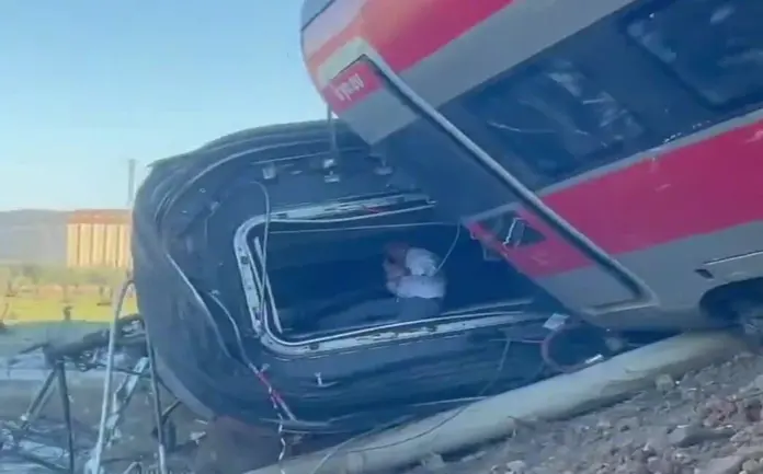 La tragedia en Urda deja un balance medio de medio centenar de heridos y 68 fallecidos FOTOGRAFÍA. URDA (TOLEDO), 28 DE OCTUBRE DE 2026. Un viajero superviviente de la colisión ferroviaria, vestido con camisa blanca de manga corta y pantalón oscuro, permanece conmocionado e inmovilizado dentro de la estructura metálica del pasadizo de interconexión de los vagones del tren Iryo, cuyo chasis ha quedado volcado y volado sobre el talud de la vía de alta velocidad. Al fondo se divisa la vegetación de la zona, mientras la chapa retorcida y el fuelle del convoy muestran la gravedad del choque ocurrido este miércoles. Lasvocesdelpueblo (Ñ Pueblo)
