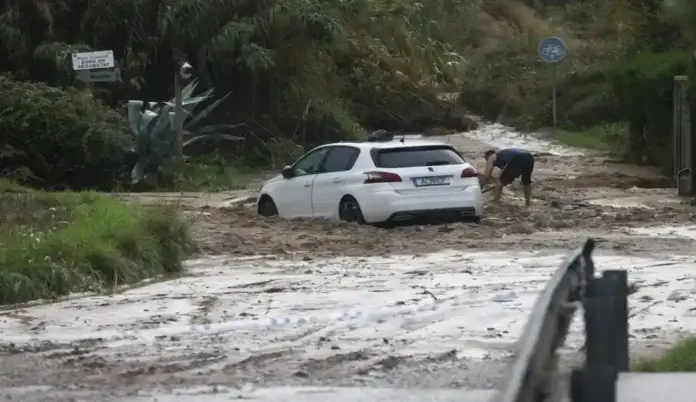 Las tormentas dejan sin electricidad a miles de hogares catalanes FOTOGRAFÍA. RONDA SUR DE GRANOLLERS, 05 DE OCTUBRE DE 2026. Un coche de color blanco de la marca Peugeot ha quedado completamente atrapado en mitad de una densa riada de barro y lodo que ha anegado la calzada tras las intensas precipitaciones acumuladas en las últimas horas en Cataluña. Junto a la parte trasera del turismo, un vecino con pantalones cortos intenta retirar desesperadamente los sedimentos acumulados con la ayuda de una pala, tratando de liberar las ruedas del vehículo en un entorno rural rodeado de cañas y vegetación salvaje donde se aprecia una señal de tráfico de carril bici. El terreno muestra los estragos de las inundaciones provocadas por el temporal que mantiene activado el plan Inuncat, con el camino totalmente cubierto por una capa de lodo marrón y un cordón policial en primer término que prohíbe el paso a la zona afectada. EFE