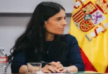 FOTOGRAFÍA. MADRID, 19 DE OCTUBRE DE 2026. La dirigente patriota y número dos de Vox al Congreso por Madrid, Montserrat Lluís Serret (Montse Lluis), sentada en una mesa de trabajo con las manos entrelazadas sobre una libreta, ataviada con jersey oscuro y luciendo una pequeña cruz en el cuello, en un acto de la formación precedido por la bandera nacional de España. Lasvocesdelpueblo (Ñ Pueblo)
