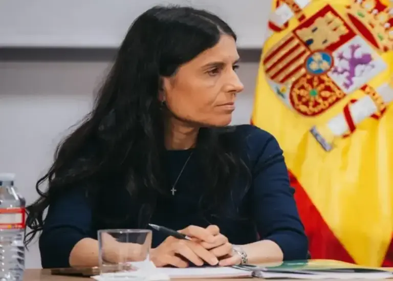 FOTOGRAFÍA. MADRID, 19 DE OCTUBRE DE 2026. La dirigente patriota y número dos de Vox al Congreso por Madrid, Montserrat Lluís Serret (Montse Lluis), sentada en una mesa de trabajo con las manos entrelazadas sobre una libreta, ataviada con jersey oscuro y luciendo una pequeña cruz en el cuello, en un acto de la formación precedido por la bandera nacional de España. Lasvocesdelpueblo (Ñ Pueblo)