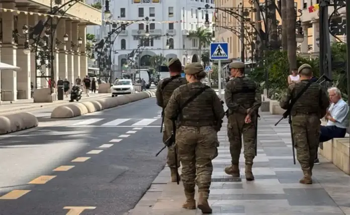 Un inmigrante ilegal ataca con cuchillo a un patrullero militar en el puerto de Ceuta FOTOGRAFÍA. CEUTA, 18 DE OCTUBRE DE 2026. Cuatro militares del Ejército de Tierra ataviados con uniforme de campaña, boina y armamento a la espalda patrullan a pie por una céntrica acera de la ciudad autónoma de Ceuta, bajo la mirada de un ciudadano mayor sentado en un banco de piedra, en una calle custodiada por banderas de España y edificios con soportales. EFE